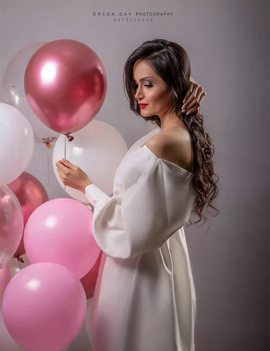 Woman in a white outfit holding a pink balloon during a birthday portrait session