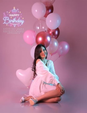 Birthday portrait of a woman in white with pink balloons and coloured studio lighting