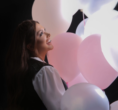 Birthday portrait in profile with pink and white balloons against a dark background