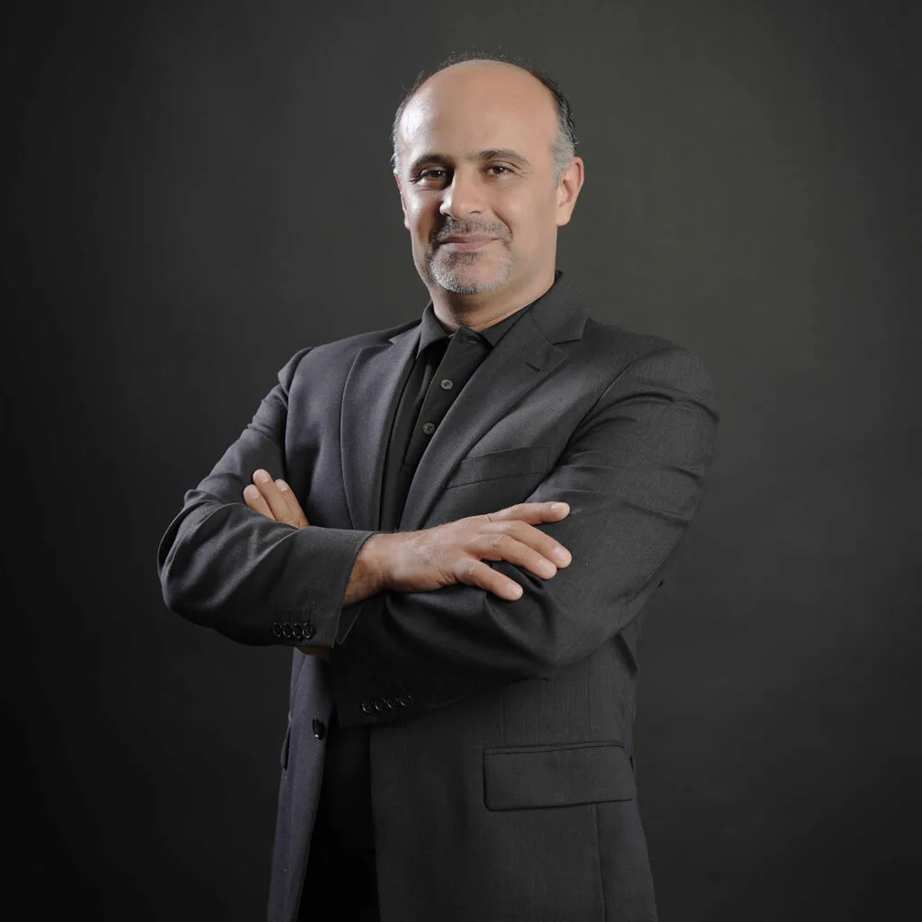 Business portrait of a man in a dark suit with folded arms against a grey background