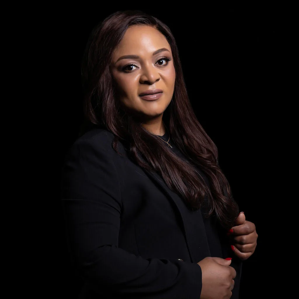 Woman in a black blazer photographed against a dark studio background