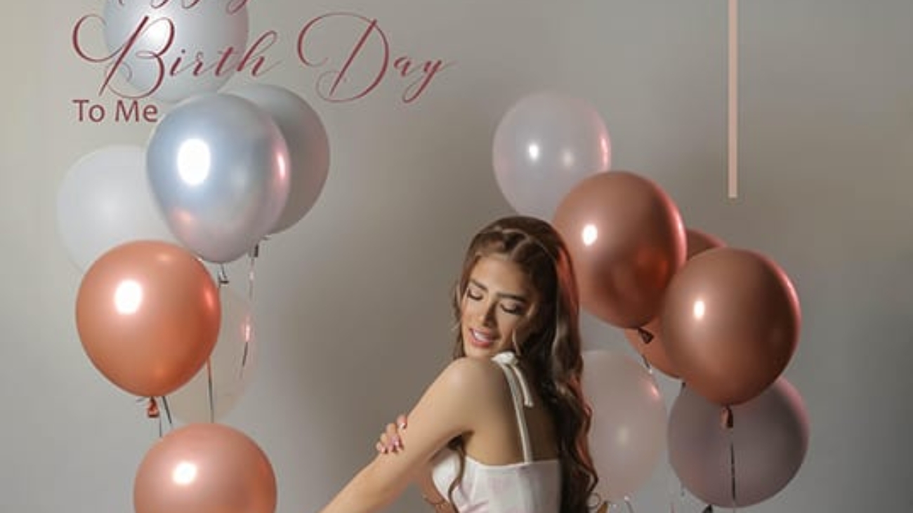 Woman in a pink skirt seated among pink, rose-gold and silver balloons during a birthday portrait session