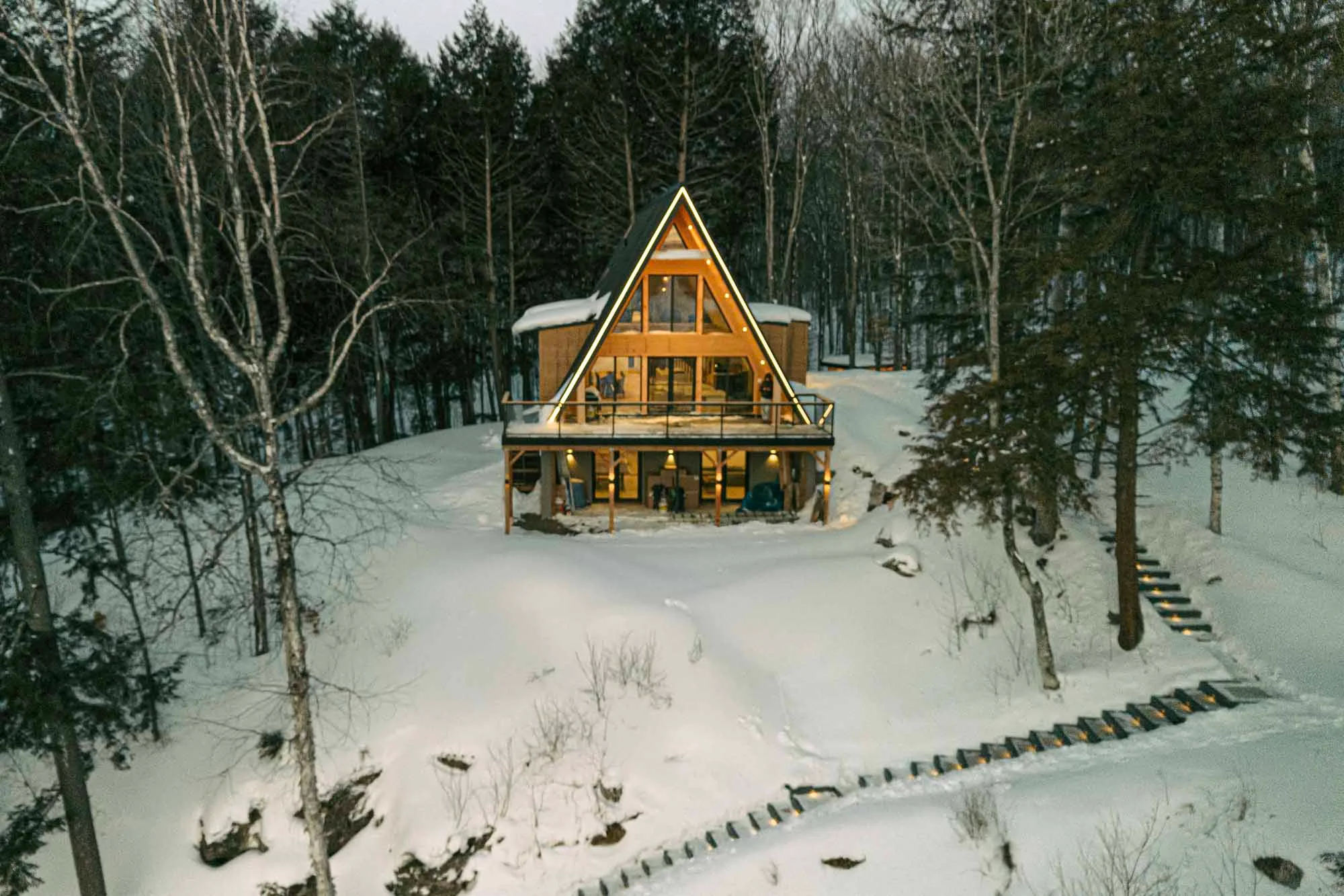Aerial drone photograph of a modern A-frame property surrounded by winter forest