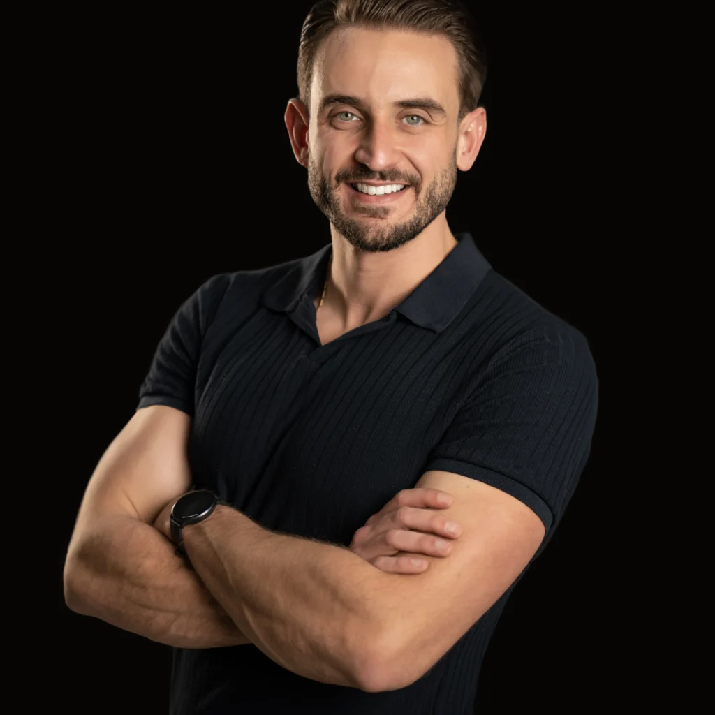 Smiling man in a black polo photographed against a black background for a professional headshot
