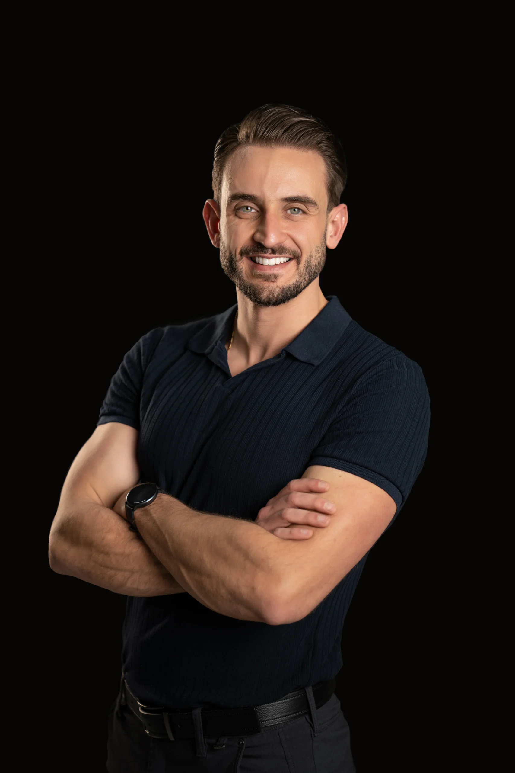 Smiling male professional with folded arms in a black-background business portrait