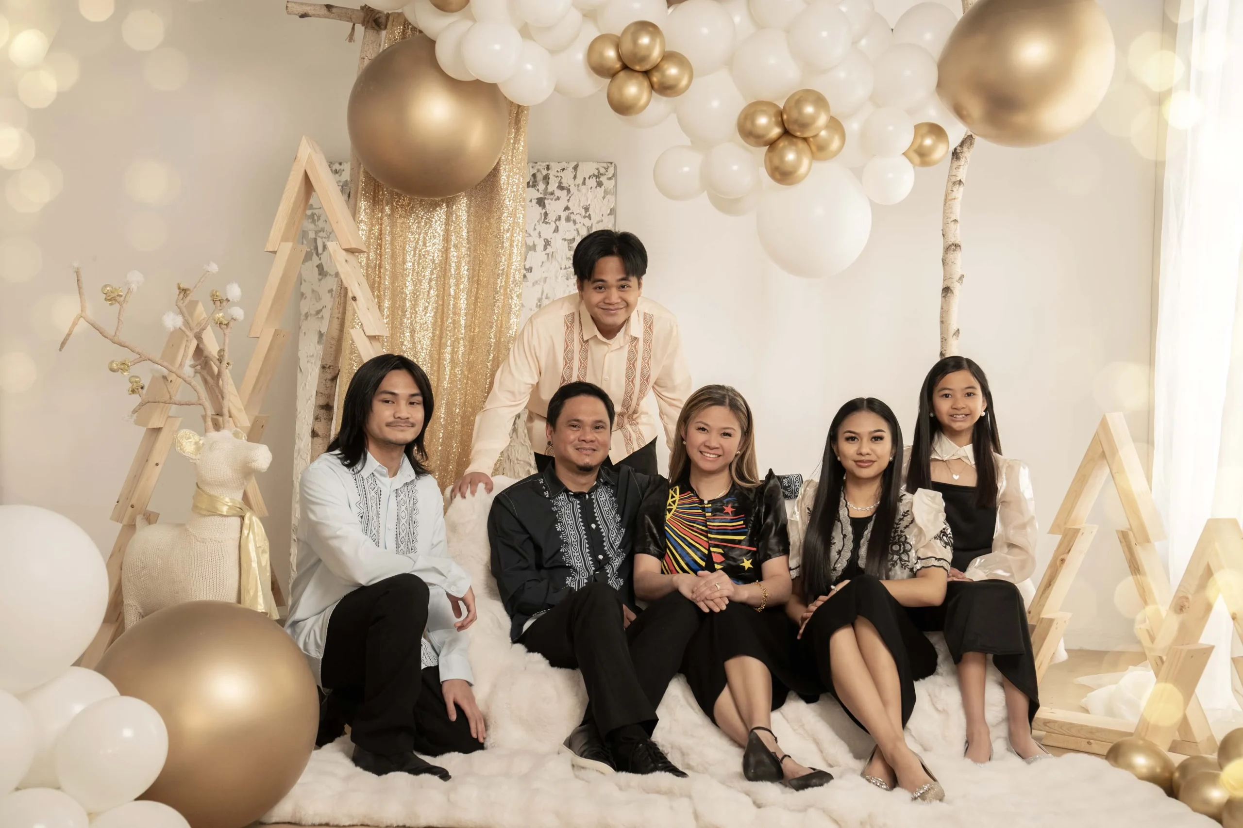 Family posing together in a cream and gold Christmas set with decorated trees and festive ornaments
