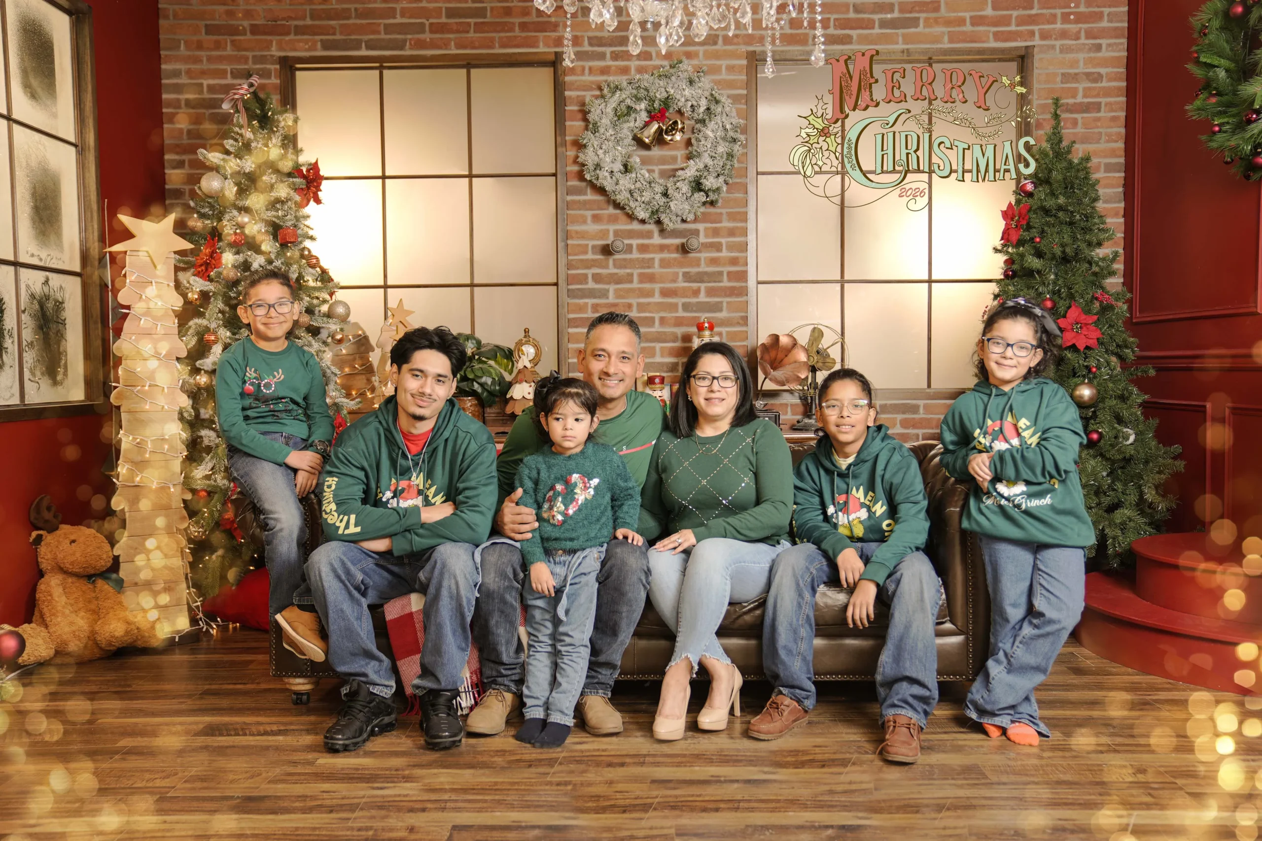 Family wearing coordinated green outfits seated together in a warm Christmas studio setting