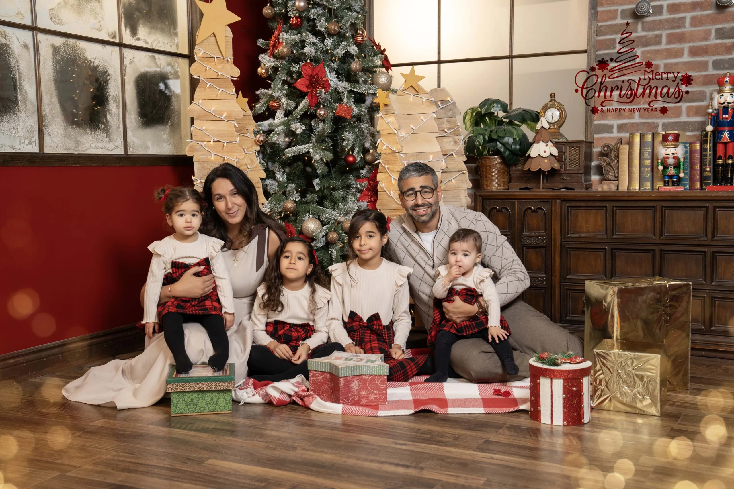 Parents and four children in cream and red plaid outfits seated beside a Christmas tree and wrapped gifts