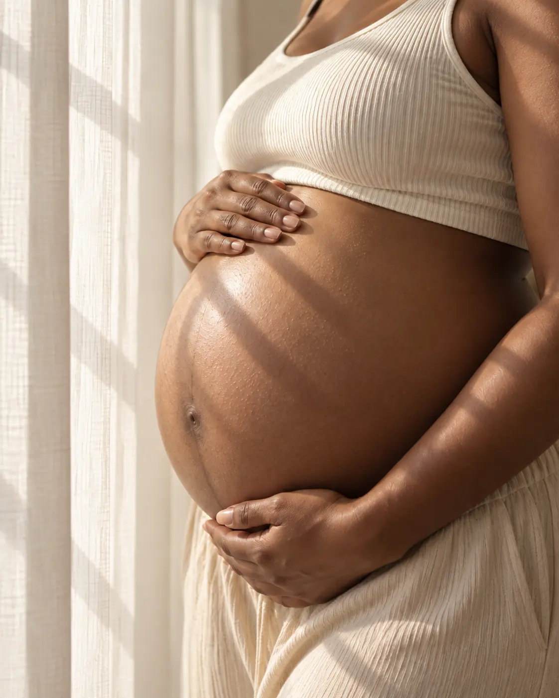 Maternity belly detail with soft window shadows in Markham
