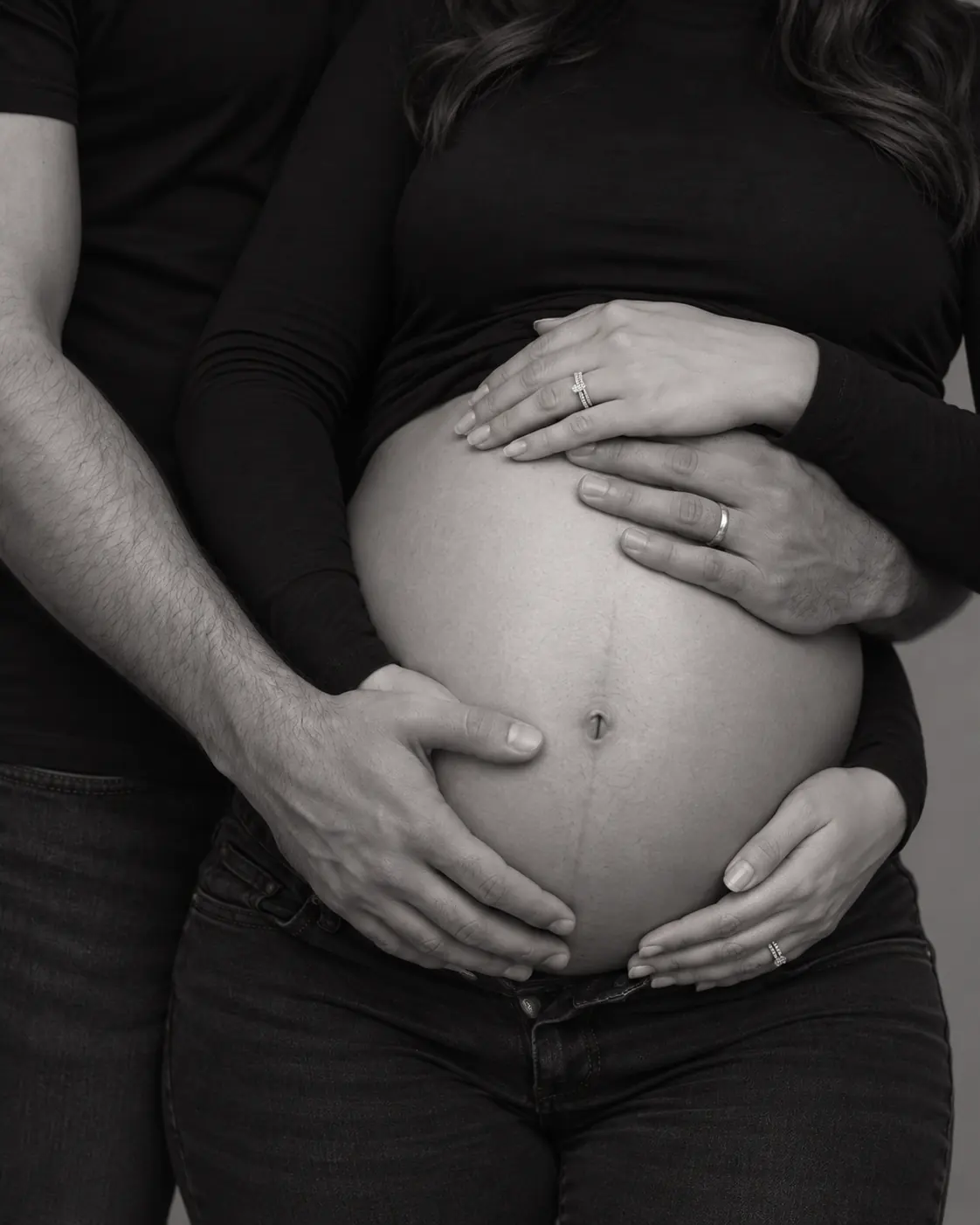 Black-and-white maternity detail of a couple’s hands around the baby bump