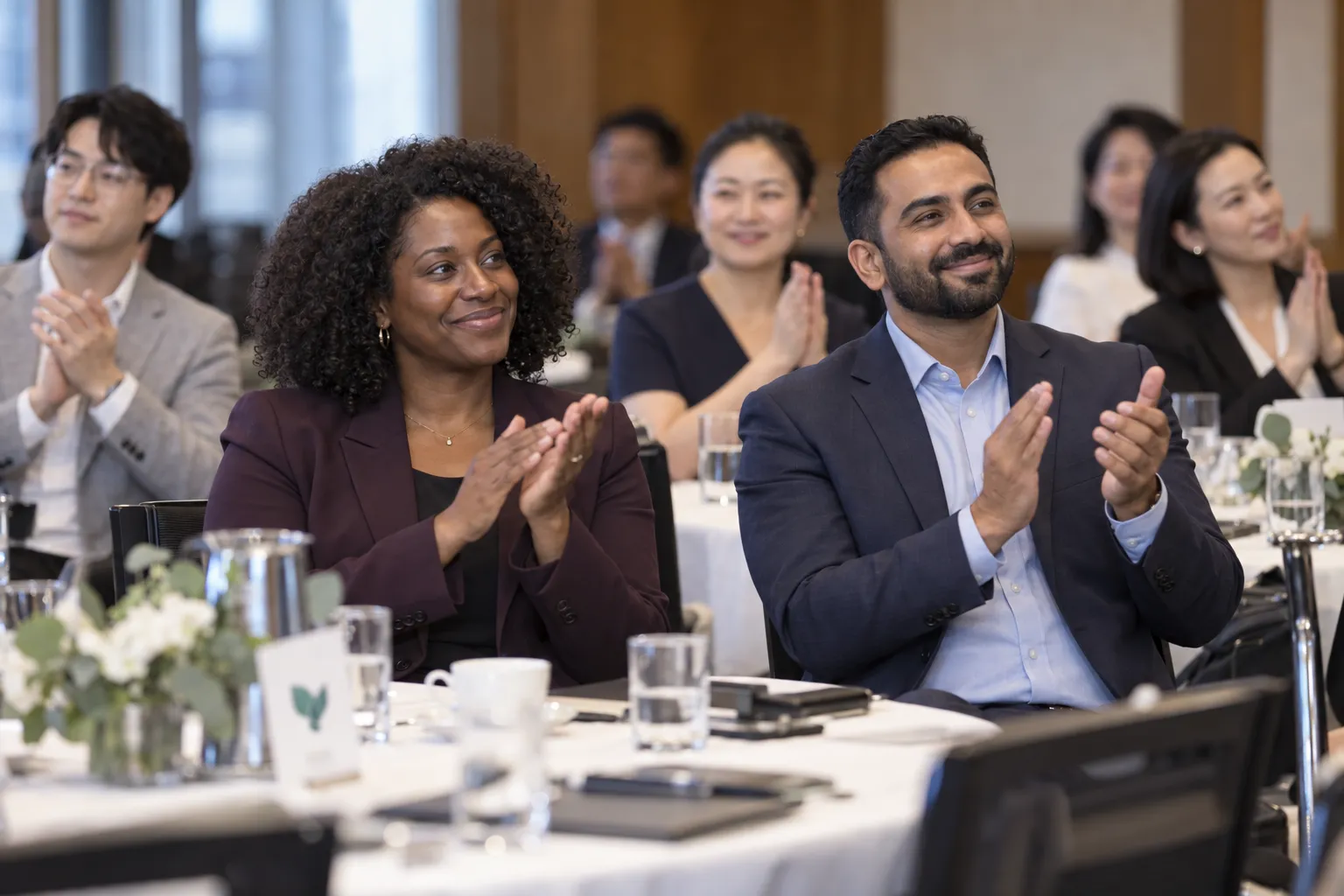 Seated attendees applauding and smiling during an indoor event