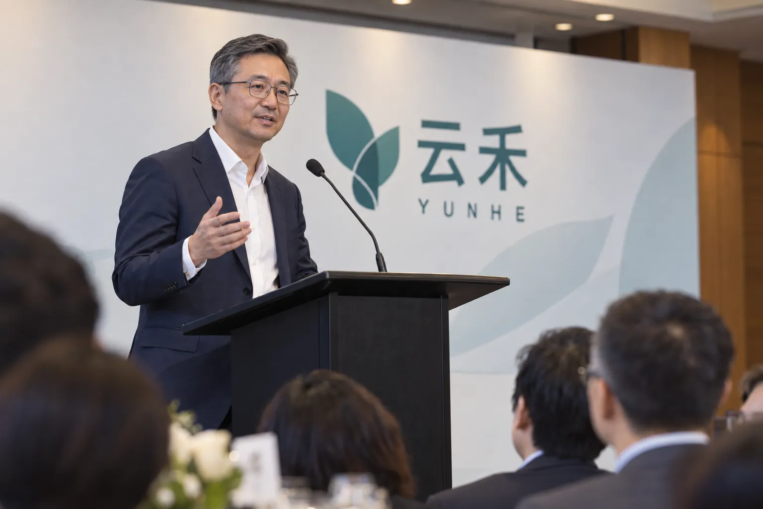 Speaker addressing seated guests from a lectern with a branded backdrop