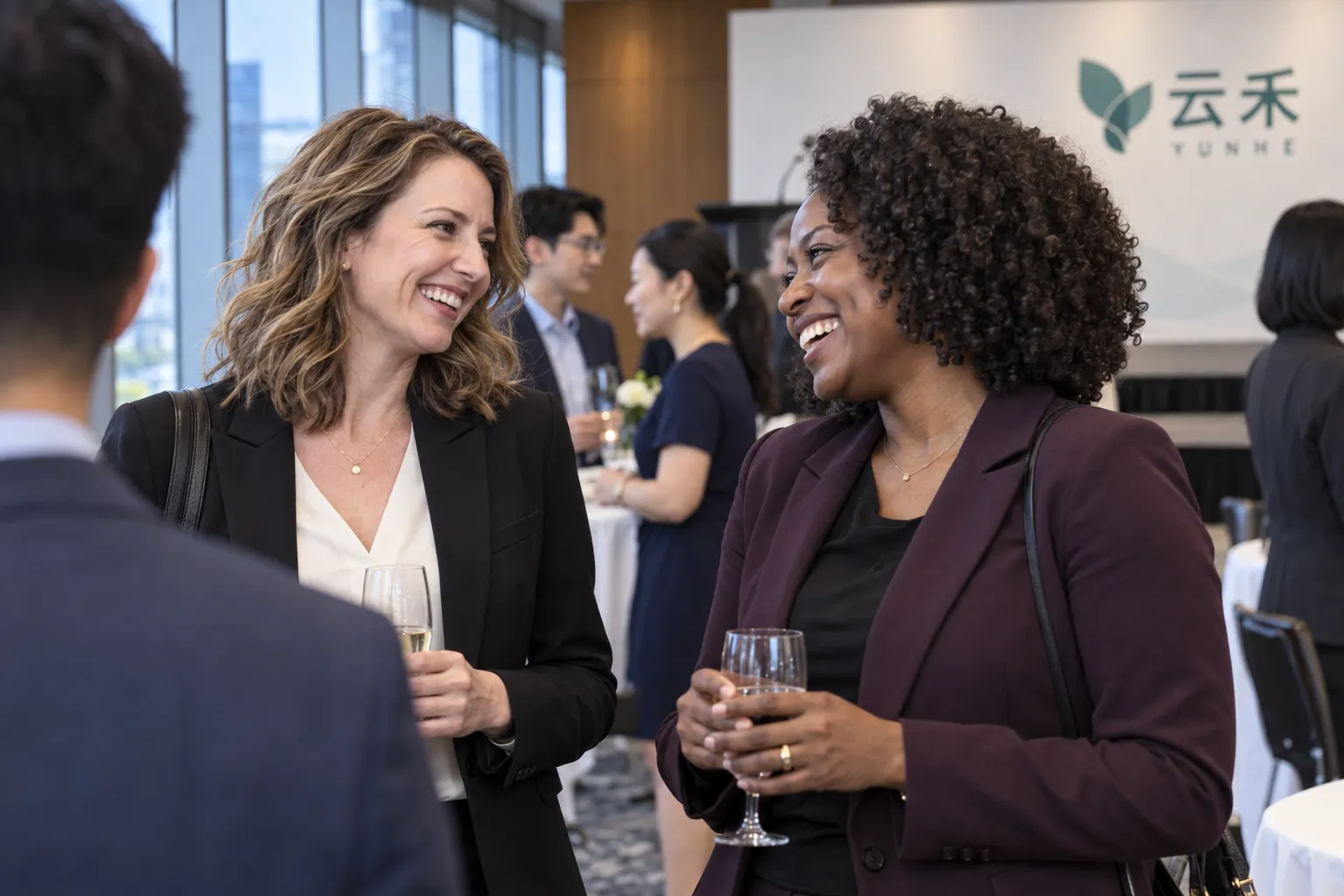 Two attendees chatting and smiling while holding drinks at an indoor reception
